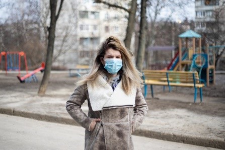 Woman standing in front of playground, wearing a medical mask